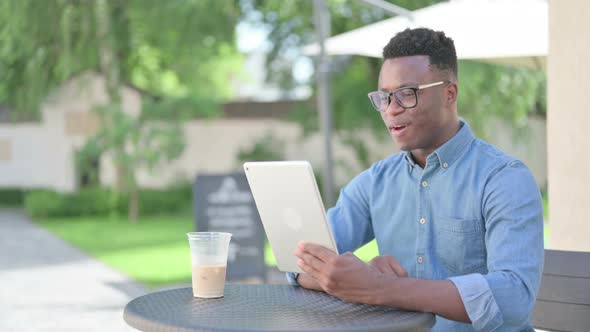 African Man Making Video Call on Tablet in Outdoor Cafe