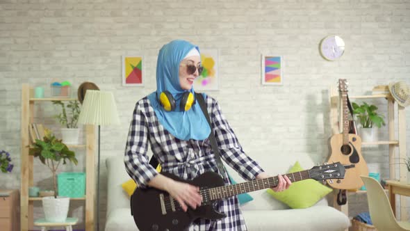 Portrait of a Cheerful Muslim Young Woman in Hijab Playing an Electric Guitar at Home