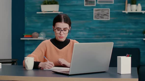 Young Person Taking Notes on Textbook and Talking on Videocall alt