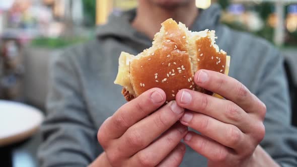 A Man Holds a Bitten Sesame Hamburger on His Outstretched Arms and Slowly Turns It in Front of the