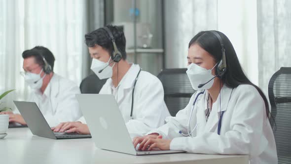 Three Asian Doctors With Stethoscopes In Headsets And Masks Working As Call Centre Agent