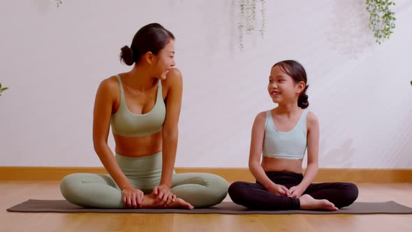 Happy Asian mom and little girl sitting on yoga mat smile and laughing together ready to exercise yo