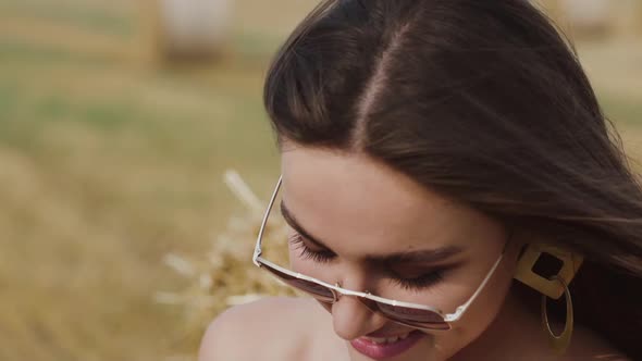 Woman in Sunglasses with Blowing Hair Looking Into Distance with Smile in Field