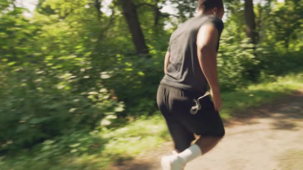 Muscular Afro Man Running in Morning Through Green Forest