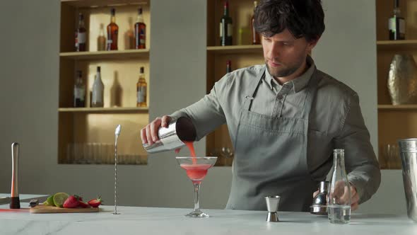 Bartender Pours a Cocktail in a Margarita Glass Decorates the Glass with Lime and Strawberries