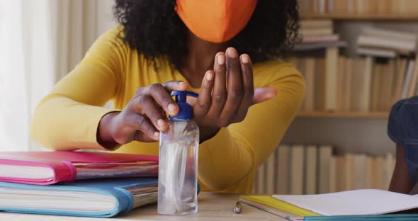 African american mother and daughter wearing face mask sanitizing their hands at home