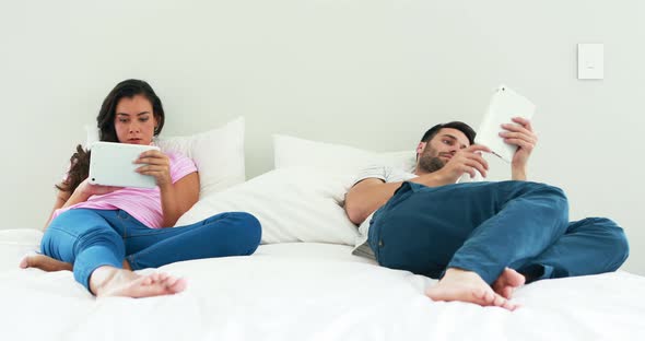 Couple using digital tablet on bed in the bedroom