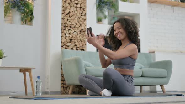 Video Chat on Smartphone By Young African Woman SSitting on Yoga Mat