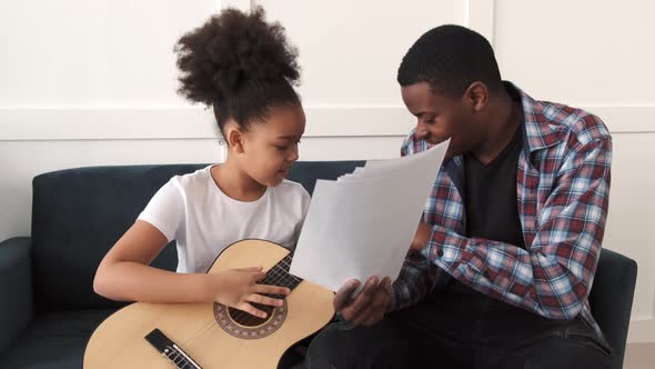 AfricanAmerican Man Teaching His Little Daughter to Play Guitar at Home