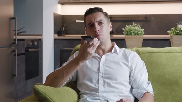 Young Man Resting on Sofa Holding Smartphone Calling Using Speaker Phone. Cheerful Male Using Mobile