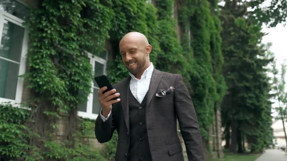 Bearded Successful Businessman Is Walking Down on Street or Park Outdoor and Using Mobile Phone