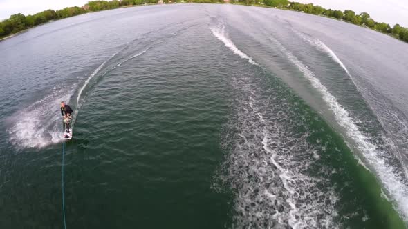 Aerial birds-eye drone view of a man wakeboarding behind a boat.