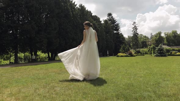 Beautiful Stylish Bride in White Wedding Dress and Veil Holding Wedding Bouquet in Hands in Park