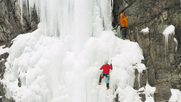 Extreme climbers scale frozen cascade side of cliff