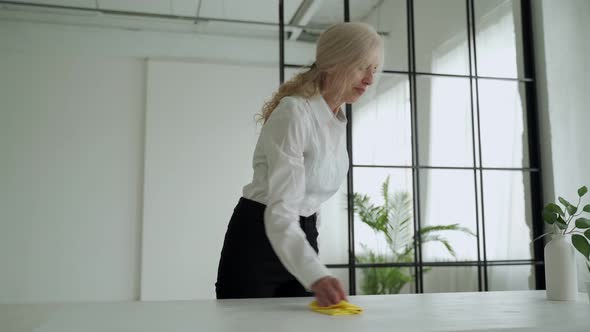 Mature Woman Wipes a Wooden Table with a Rag