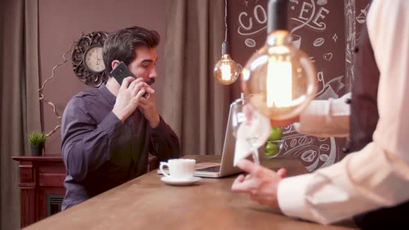 Man Answers a Phone Call While Working on His Computer and Drinking Coffee