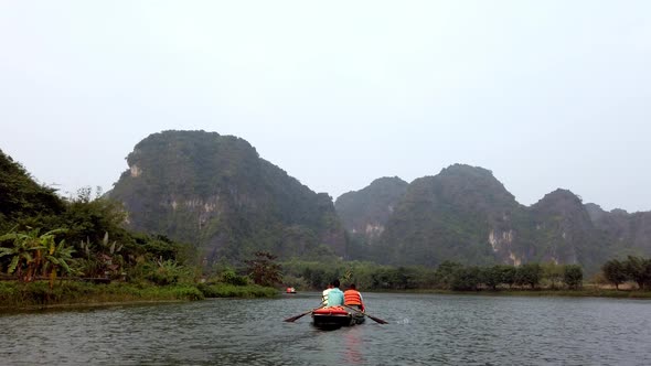 Tour boat with tourists and guide paddling on Day River overlooking limestone Kerst mountain landsca