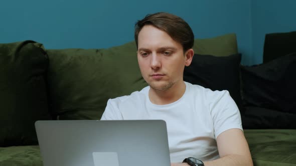 Portrait of a Young Man Sitting Near Sofa with Laptop Working From Home