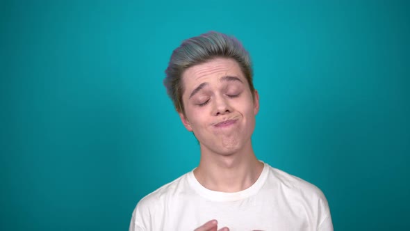 Young Smiling Man with Color Hair Say OOPS Shrugs Isolated on Blue Background