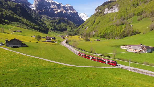Aerial footage of a train passing through snow capped mountain in Switzerland on a sunny day