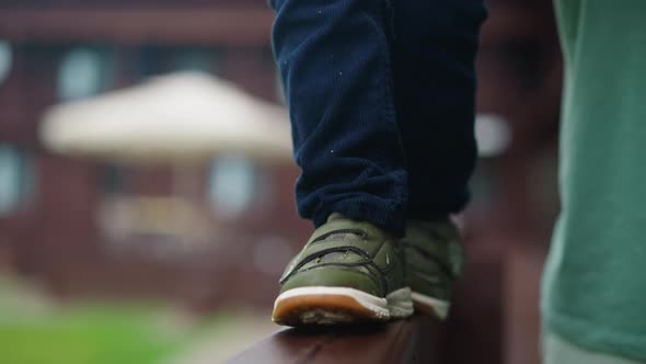 Toddler Boy in Green Sneakers Walks Along Wooden Railing