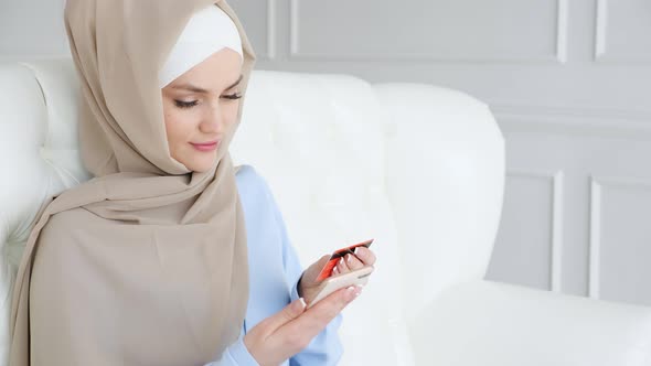 Muslim Woman in Hijab is Buying Online with a Credit Card and Smartphone
