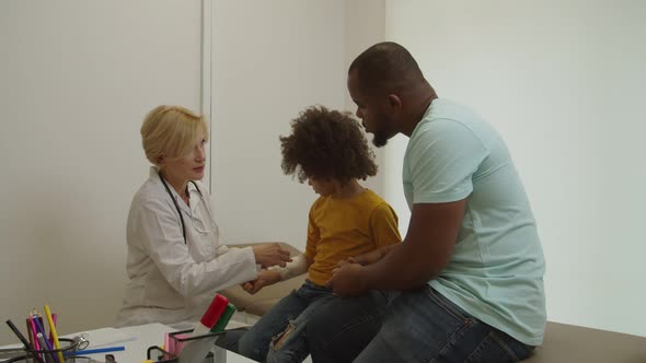 Positive Lovely Woman Doctor Applying Bandage on Injured Arm of Cute Little Kid at Hospital