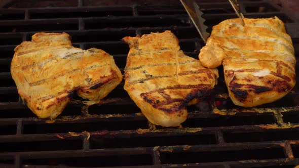 The Hand is Checking and Rotating Chicken Fillet on the Grill with Kitchen Tongs