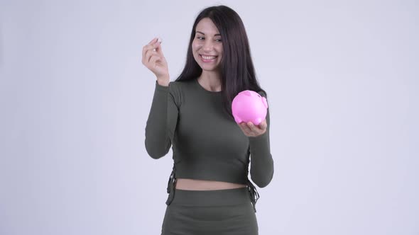 Happy Young Beautiful Woman Inserting Coin To Piggy Bank As Joke