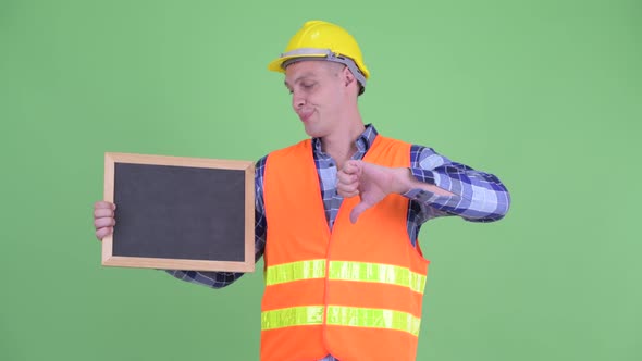 Stressed Young Man Construction Worker Holding Blackboard and Giving Thumbs Down