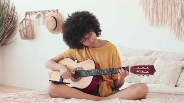 Afro American Girl Learning to Play Guitar Using Smartphone