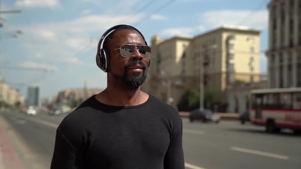 Adult Afro American Man Is Walking on Street and Listening Music By Heading at Summer Day