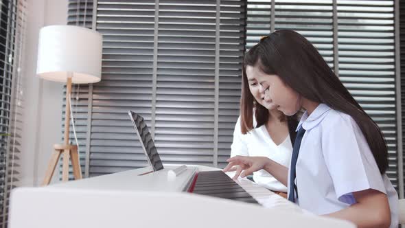 Mother helping daughter during virtual piano lesson. Digital music education concept.