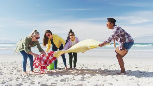 Happy group of diverse female friends having fun, preparing picnic at the beach