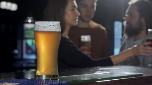 Selective Focus on a Beer Glass, People Drinking at the Pub on the Background