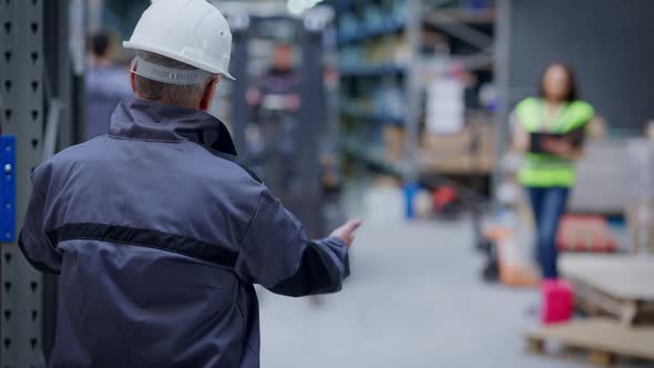 Back View of Experienced Professional Warehouse Employee Gesturing Controlling Driver Riding