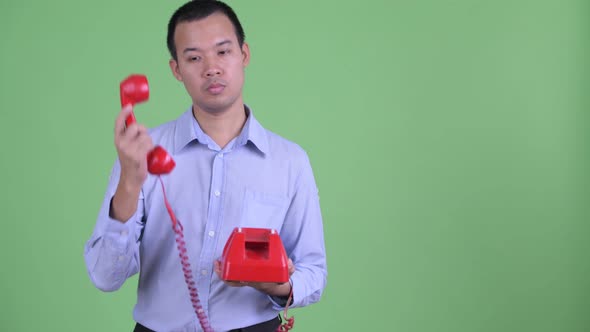 Young Businessman Giving Telephone To Stressed Asian Businessman Looking Bored