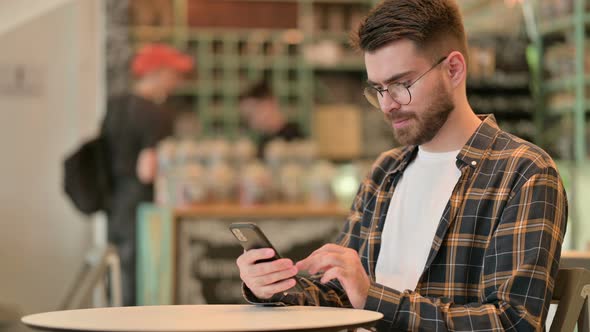 Attractive Young Man Using Smartphone in Cafe 