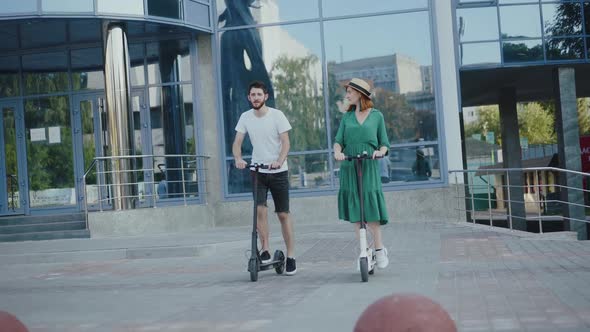 Happy Couple Riding on Electric Scooters Around Area and Having Funny Talk