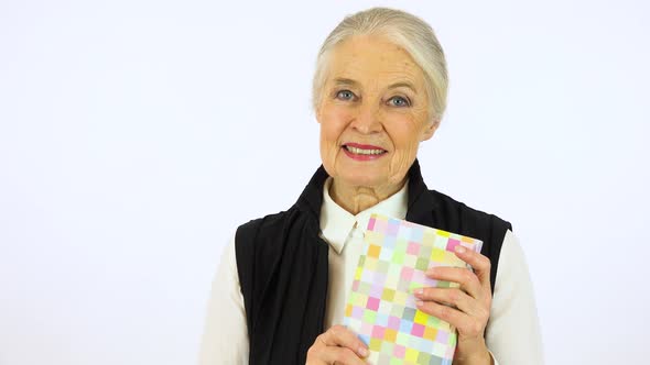 An elderly woman holds a book, smiles at it and at the camera - white screen studio