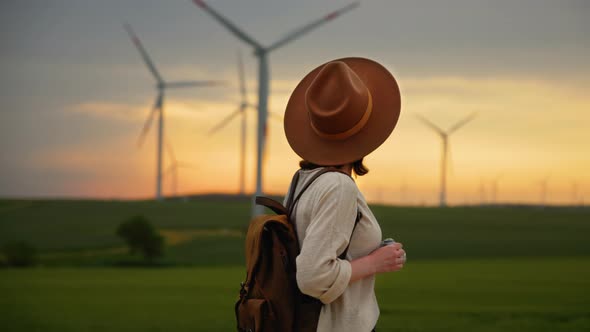 Young woman in a hat with a camera in a field with windmills