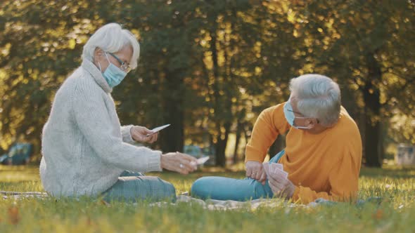 Anniversary Celebration in the Park During Covid-19. Elderly Couple with Face Maskplaying Card Game