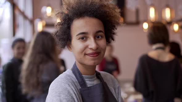 Close Up Footage of Dark Skinned Female with Afro Haircut Standing in Crowded Restaurant Smiling in