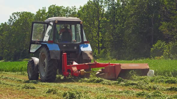 Modern tractor cuts green grass in the countryside. 