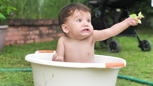 A Small Beautiful Child Sits in a Round Light Basin Holds a Flower at Arm's Length and Looks Around