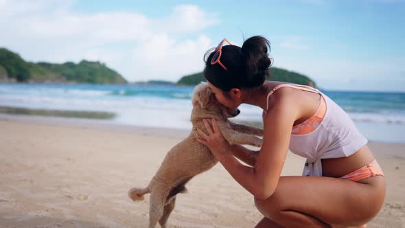 Happy Smiling Beautiful Asian Woman in Swimsuit Playing with Her Cute Dog on the Tropical Beach