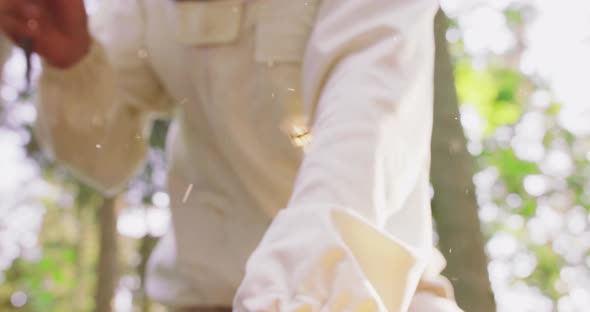 Blurred Male Beekeeper in White Protective Suit Inclined Puts the Bee Hive Tool Aside Then Takes the