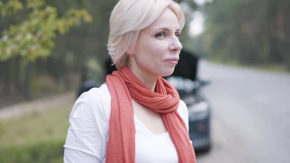 Close-up Portrait of Blond Caucasian Woman Turning From Car with Open Hood and Showing Strength