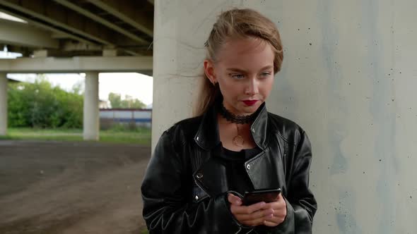 Young Girl in Black Leather Jacket Using Mobile Phone on City Street