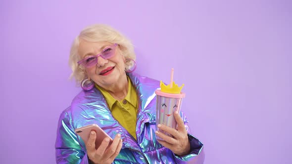 Woman with Blonde Hair in a Bright Fashionable Jacket with a Cocktail in Her Hand Takes a Selfie or